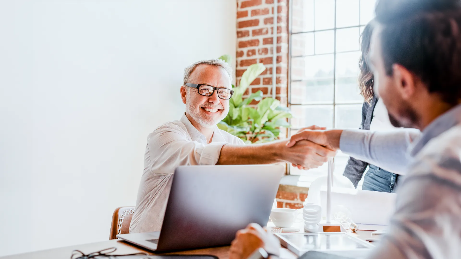 Two businessmen shaking hands over a laptop in office