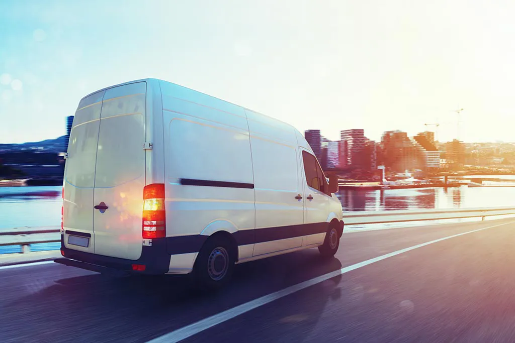 White van driving on sunny highway by city